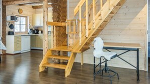 A wooden staircase leading to a loft bedroom, a kitchen with wooden cabinets, and a dining area with a table and chair. - Puljunharju by Interhome (Sodankylä)