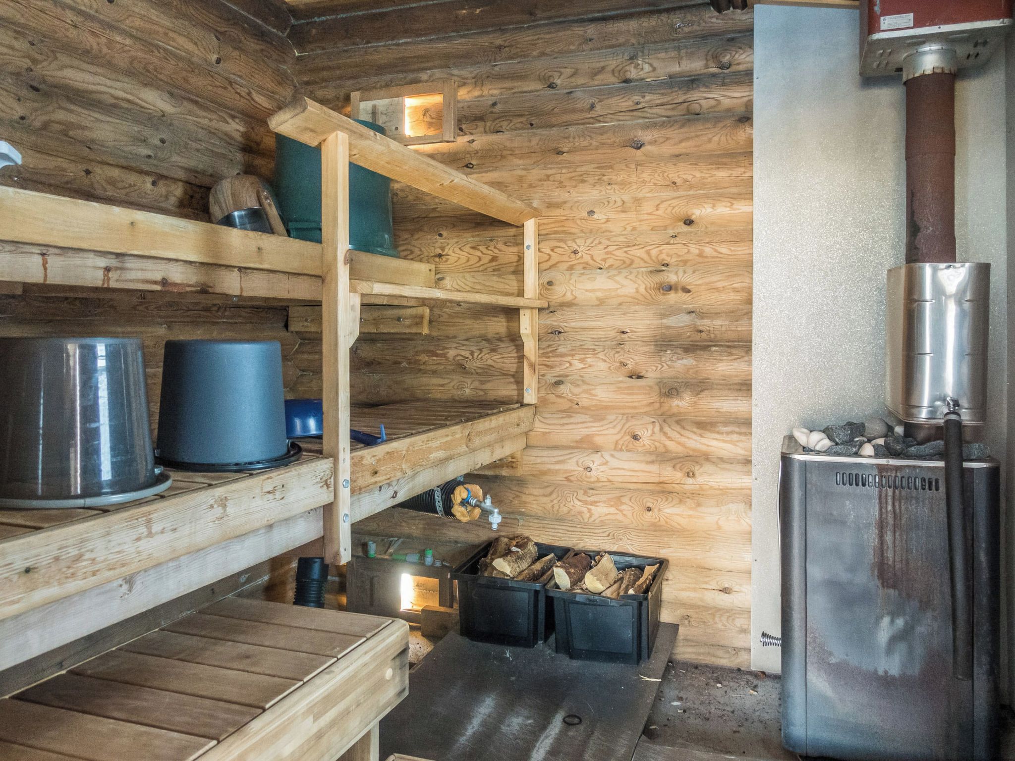 Interno di una rustica baita con pareti in legno, stufa in metallo, mensole con contenitori e una panca.