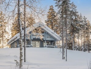 Une cabane en rondins avec un toit pentu, entourée d’arbres couverts de neige.