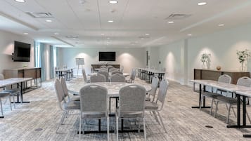 Une salle de conférence dotée de plusieurs tables et chaises, d’un téléviseur à écran plat fixé au mur et d’un sol recouvert de moquette.