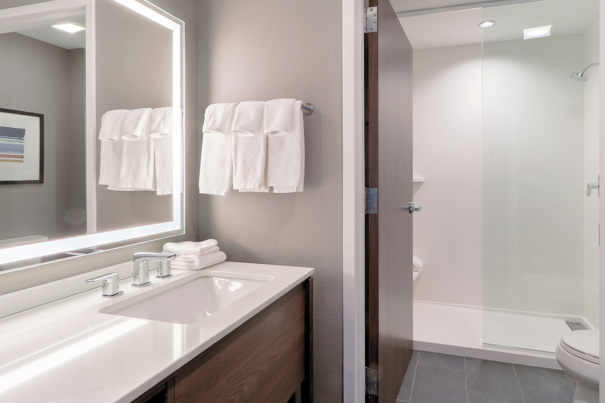 Un baño moderno con un espejo grande, un lavabo blanco y una ducha con mampara de vidrio.