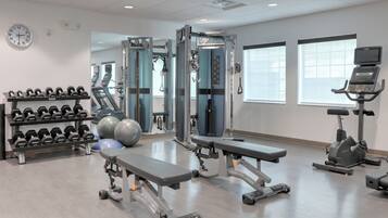 Un gimnasio con máquinas de pesas, mancuernas, cintas de correr y balones de ejercicio.