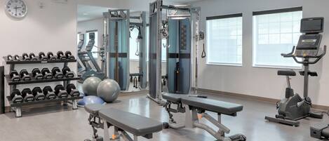 Un gimnasio con máquinas de pesas, mancuernas, cintas de correr y balones de ejercicio.
