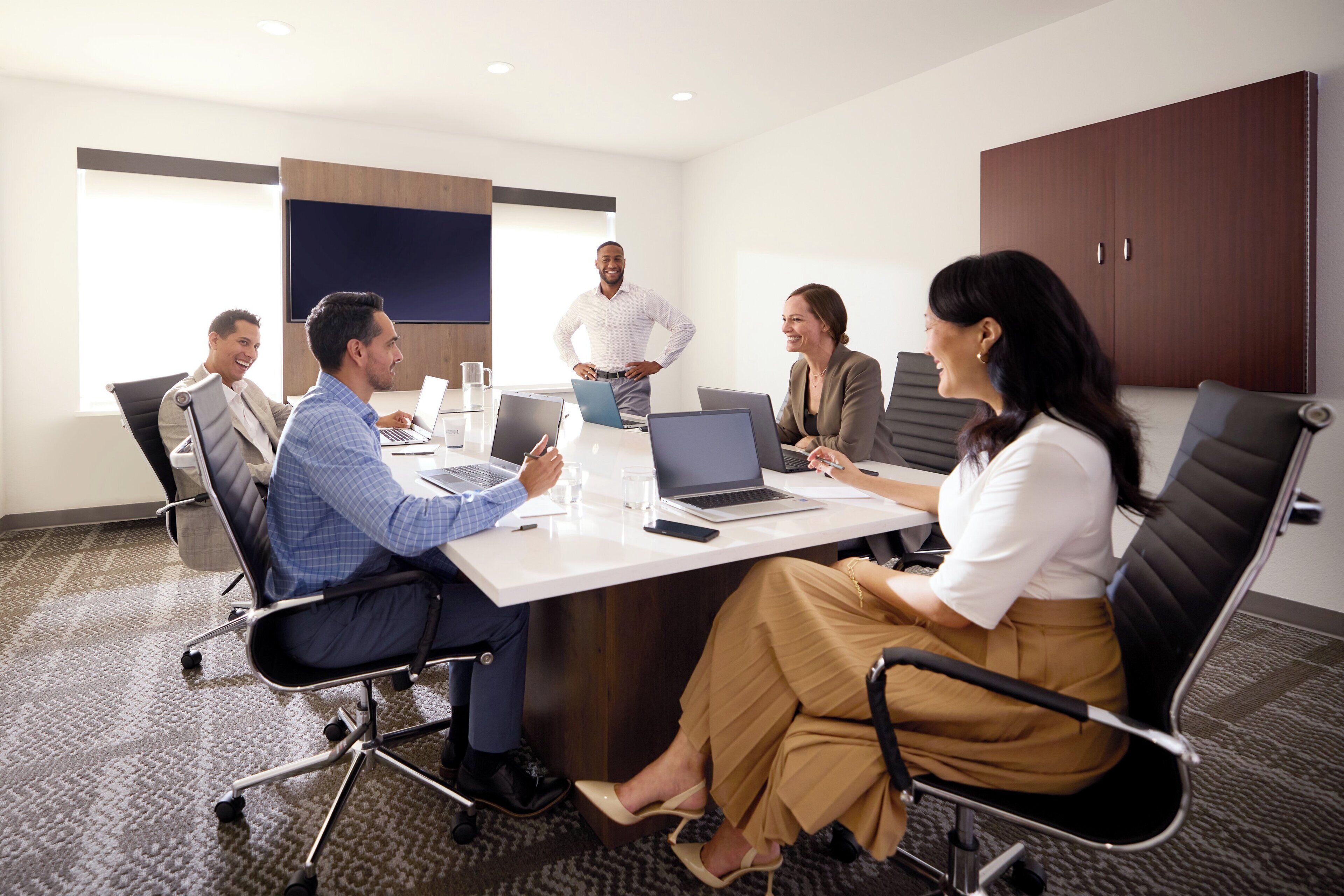 A conference room with a white table, black chairs, and a wooden cabinet.