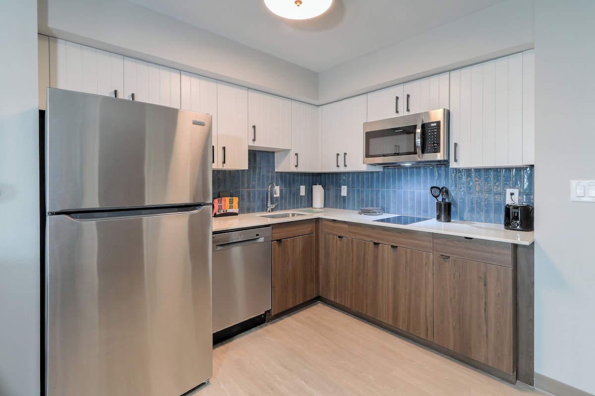 Una cocina moderna con electrodomésticos de acero inoxidable, armarios de madera y un salpicadero de azulejos azules.