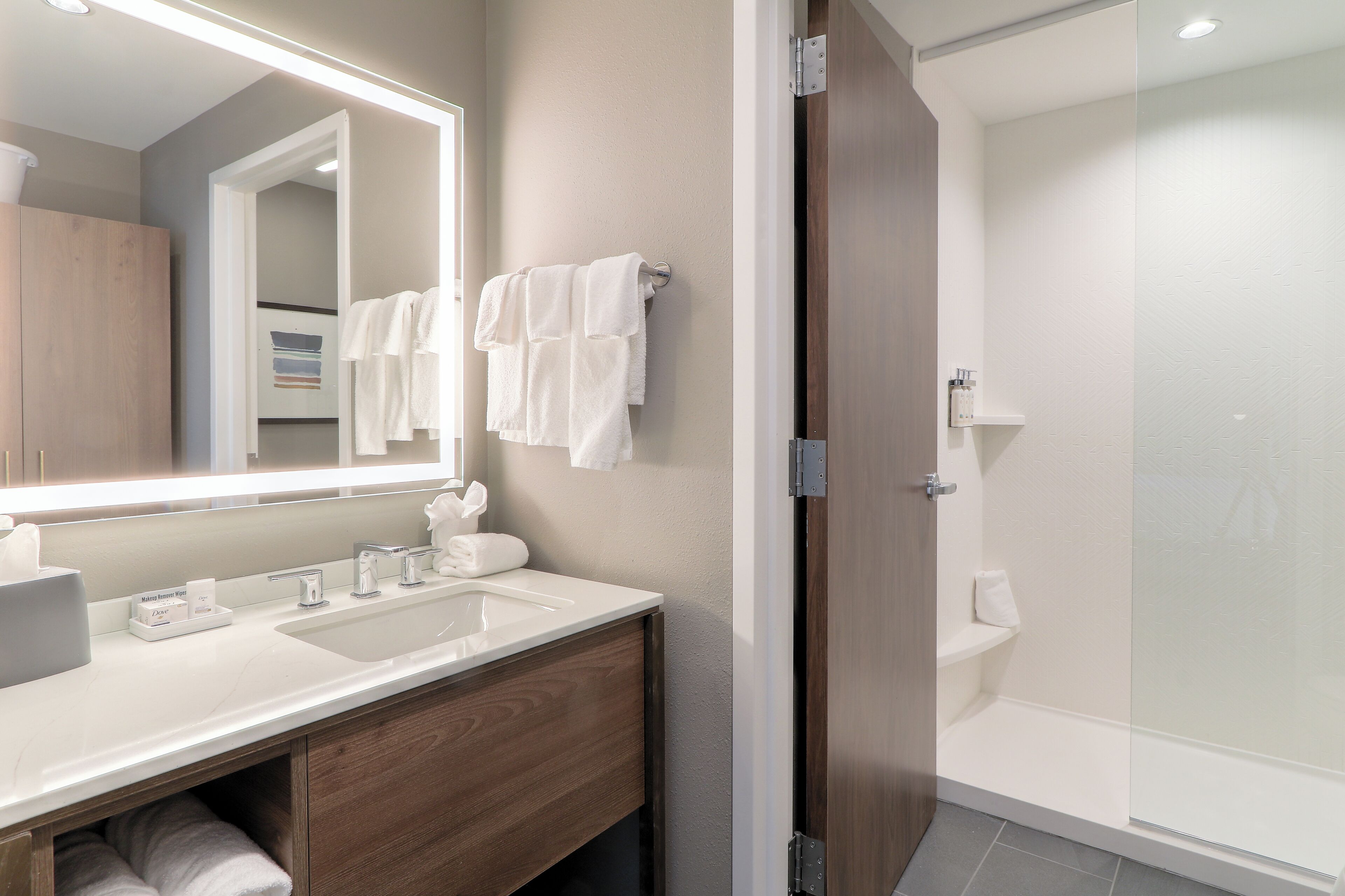 A modern bathroom with a large mirror, two sinks, and a glass-enclosed shower.