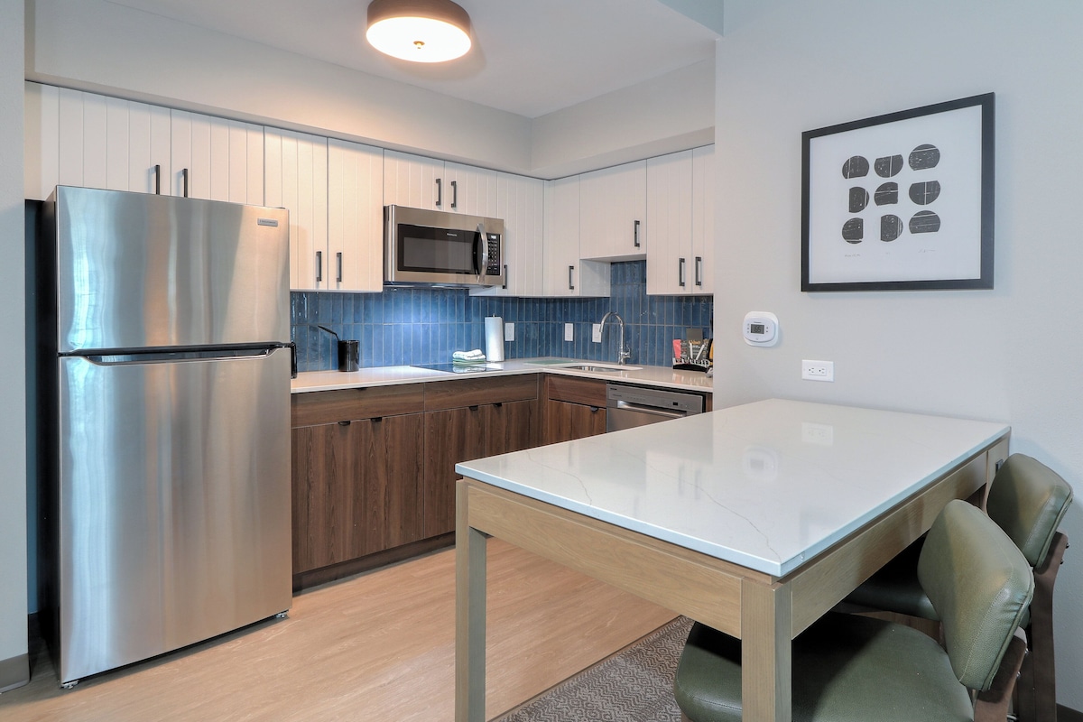 Una cocina moderna con electrodomésticos de acero inoxidable, armarios de madera y encimera de mármol.