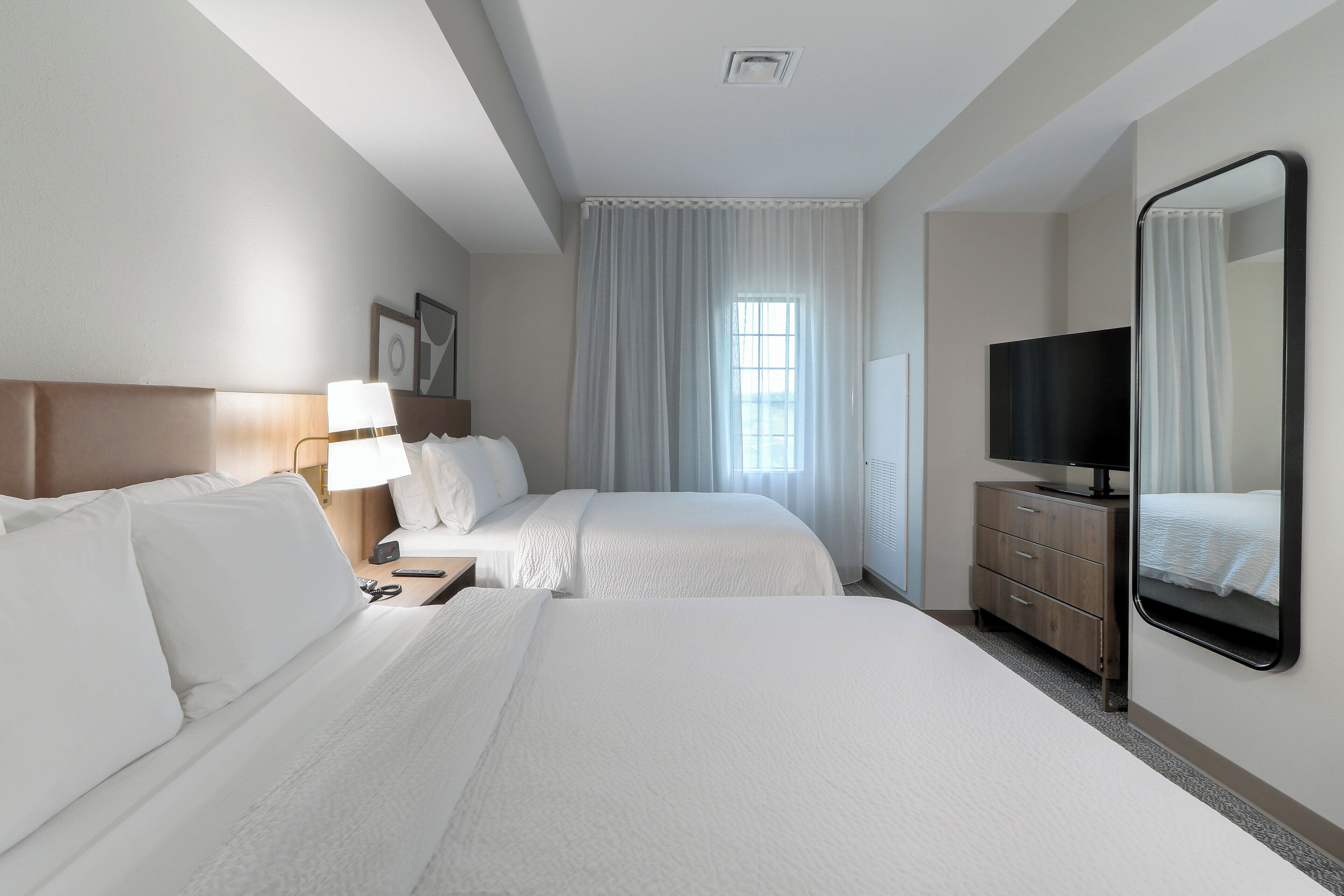 Une chambre d’hôtel avec deux lits, une télévision, une commode et une fenêtre avec des rideaux.