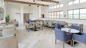 Un comedor amplio con varias mesas y sillas, ventanas grandes y un diseño moderno del techo.