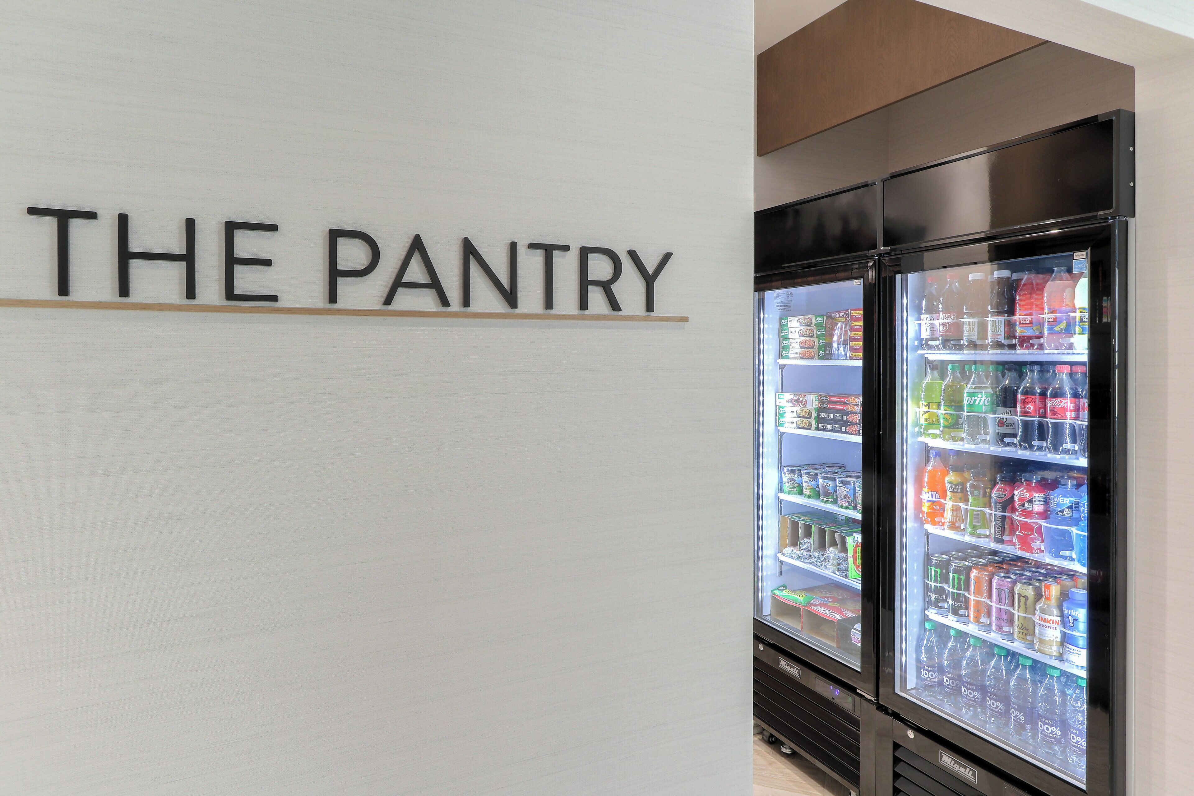 Een gekoelde vitrine met de tekst 'THE PANTRY', gevuld met diverse drankjes en snacks.