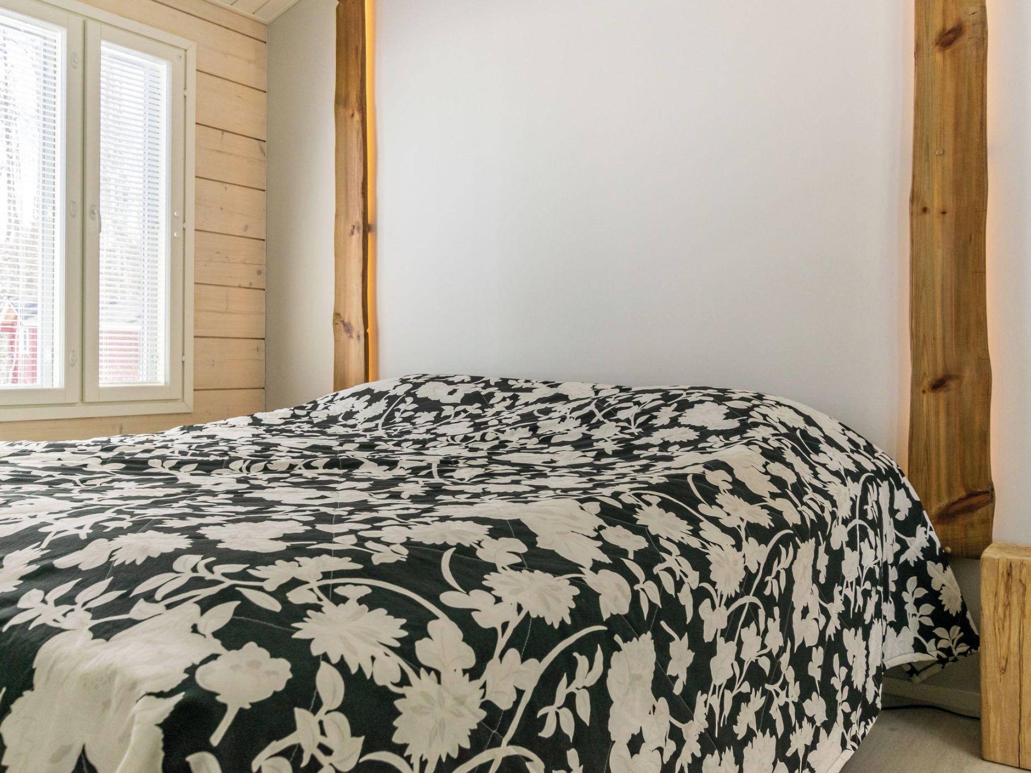 A bedroom with a bed, wooden beams, and a window with blinds.