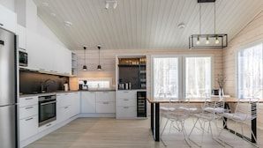 Una cocina moderna con armarios blancos, una isla central, iluminación colgante y un comedor con sillas blancas.