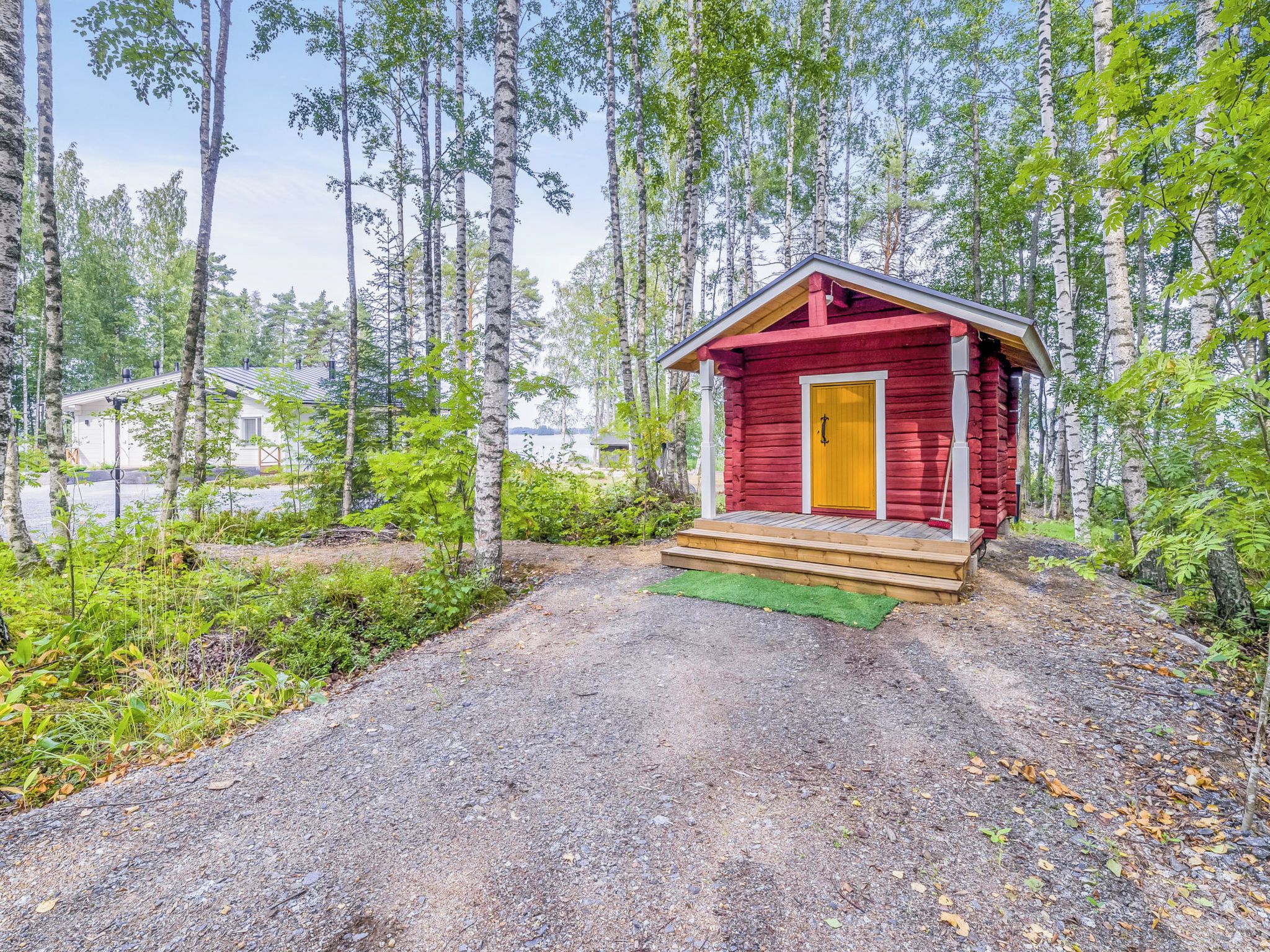 A small red cabin with a wooden porch, surrounded by a forested area.