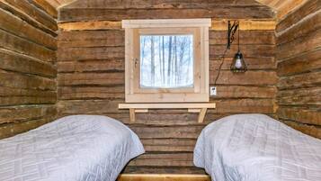 Et bjælkehytteværelse med to senge, et vindue med udsigt til træer, og en vægmonteret lampe.