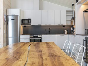 A modern kitchen with white cabinetry, a wooden dining table, and a built-in microwave.