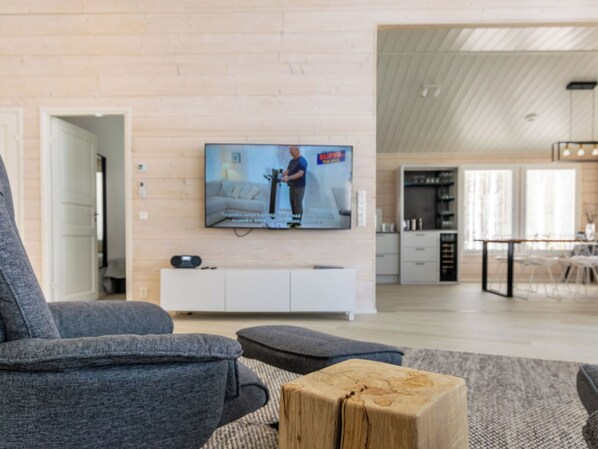 A modern living room with a flat-screen TV mounted on a light-colored wall, grey sofa, and a wooden coffee table.