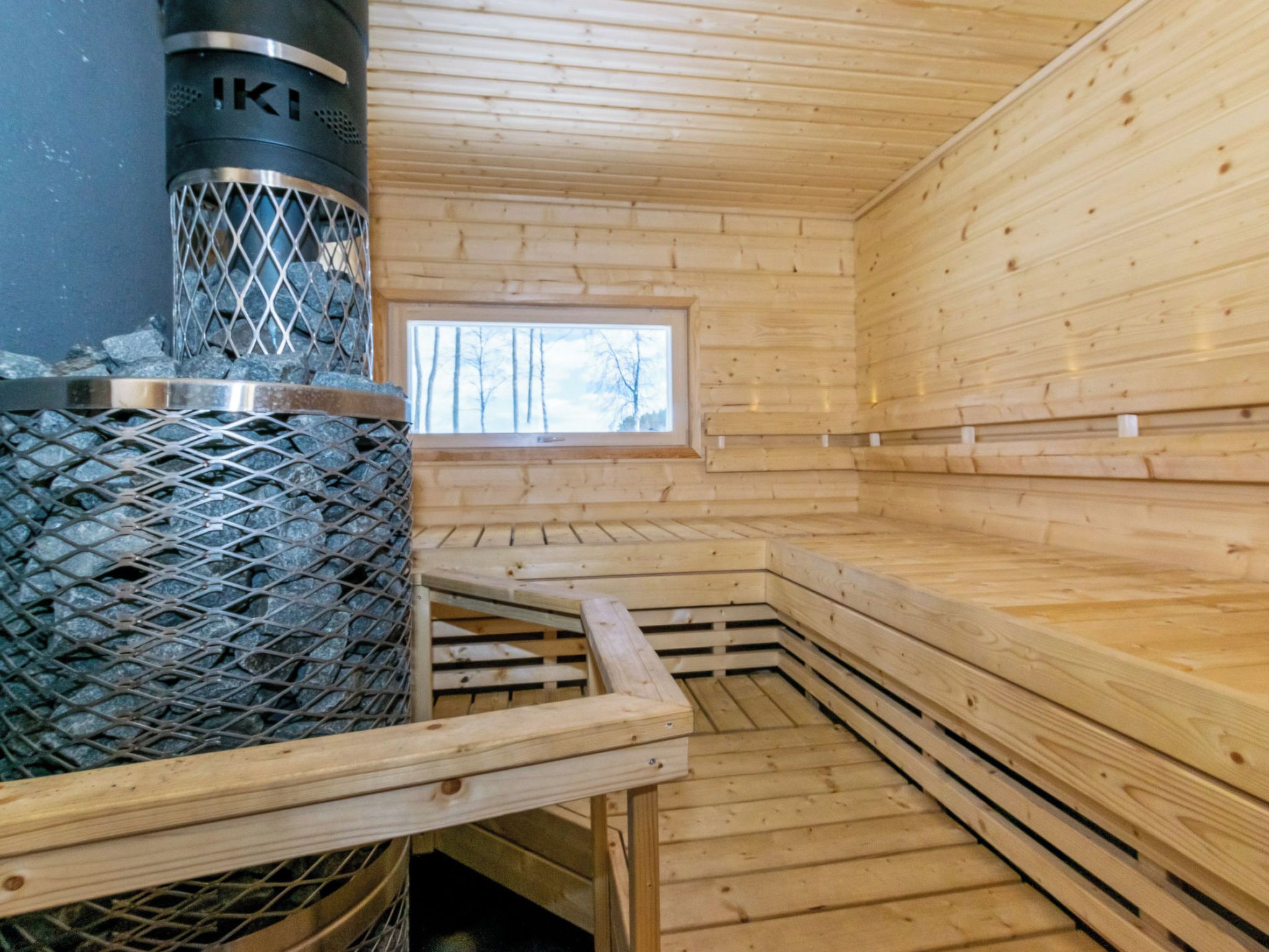 A sauna room with a metal grate stove, wooden benches, and a window.