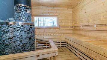 A sauna room with a metal grate stove, wooden benches, and a window.