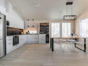 A modern kitchen with white cabinetry, stainless steel appliances, and a dining area with a wooden table and metal chairs. - Palanteen haavelinna by Interhome (Orivesi)