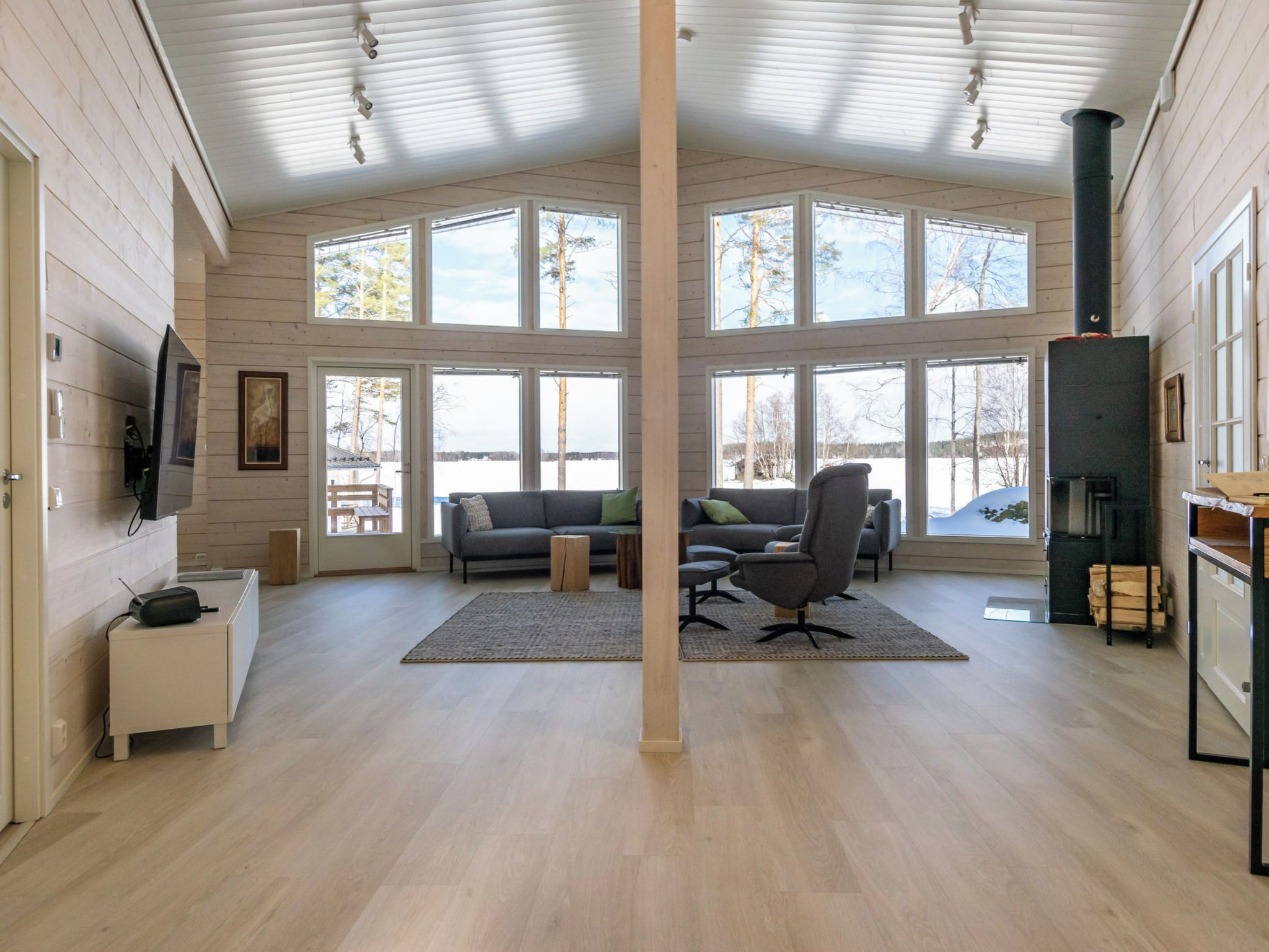 A spacious living room with a large window, a fireplace, and a television mounted on the wall.