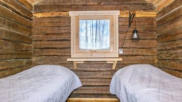 A cabin interior with two beds, a window with a view of trees, and a wall-mounted light fixture.