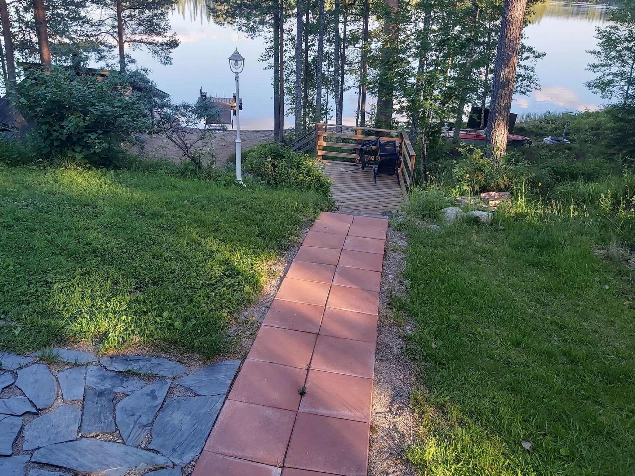 Un chemin pavé mène à une terrasse en bois d’où l’on a vue sur un lac.