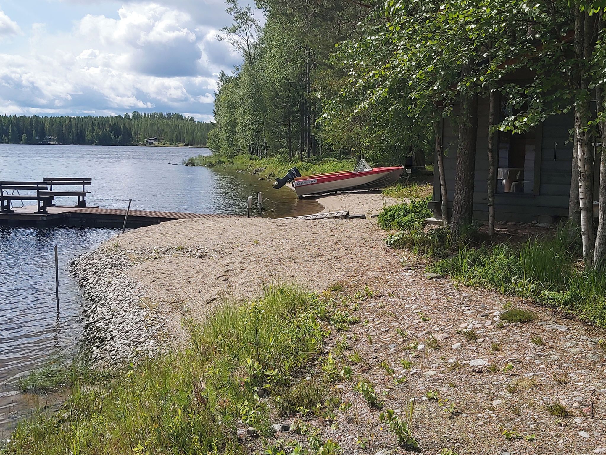 A lakeside cabin with a dock extending into the water, surrounded by trees and a picnic table.