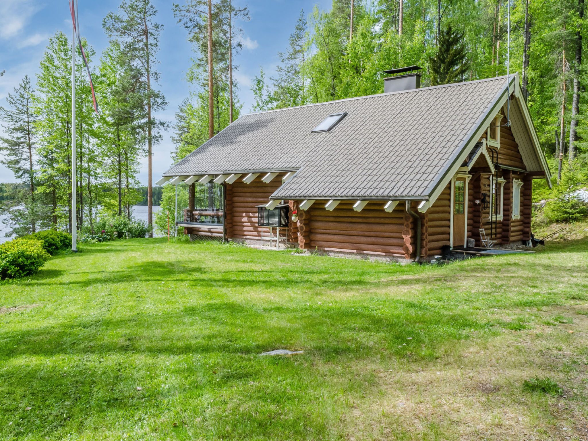 A log cabin with a sloped roof, a porch, and a view of a lake surrounded by trees.