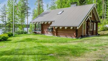 A log cabin with a sloped roof, a porch, and a view of a lake surrounded by trees.