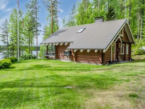 A log cabin with a sloped roof, a porch, and a view of a lake surrounded by trees.