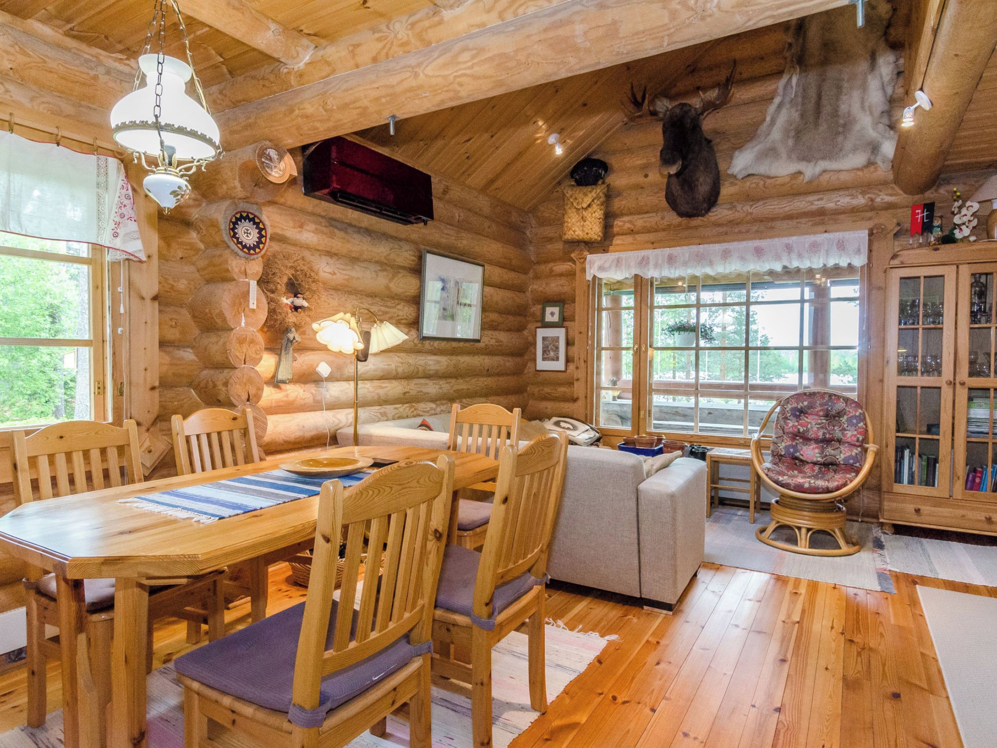 A log cabin interior with a dining area, seating, and a view of the outdoors.