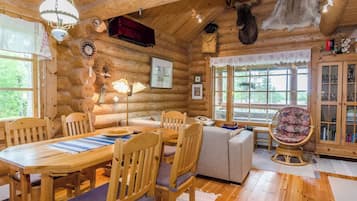 A log cabin interior with a dining area, seating, and a view of the outdoors.