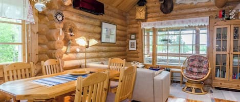 L’intérieur d’une cabane en rondins comprend un coin repas, des sièges et offre une vue sur l’extérieur.