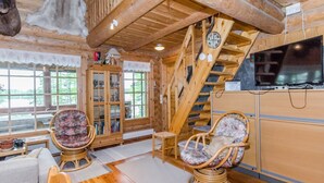 A log cabin interior with wooden floors, a staircase, a television, and two wicker chairs.