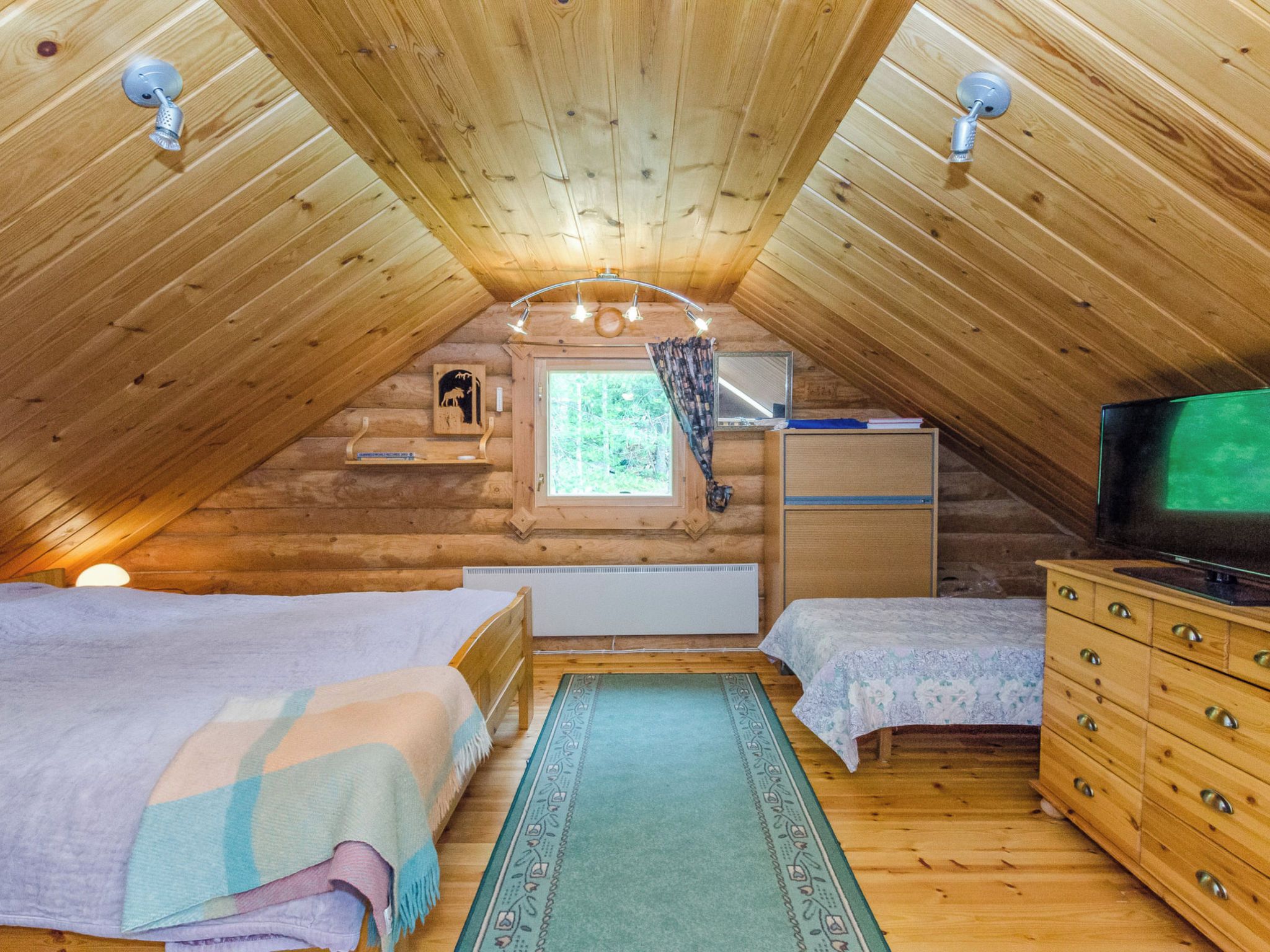 Quarto de sótão acolhedor com duas camas, uma cômoda, uma televisão e uma janela com vista para o exterior.