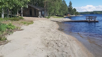 Un chemin de gravier mène à un chalet en bois situé au bord d’un lac, avec une jetée qui s’avance dans l’eau.