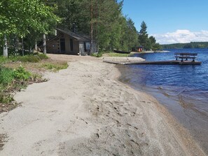 Un chemin de gravier mène à un chalet en bois situé au bord d’un lac, avec une jetée qui s’avance dans l’eau.