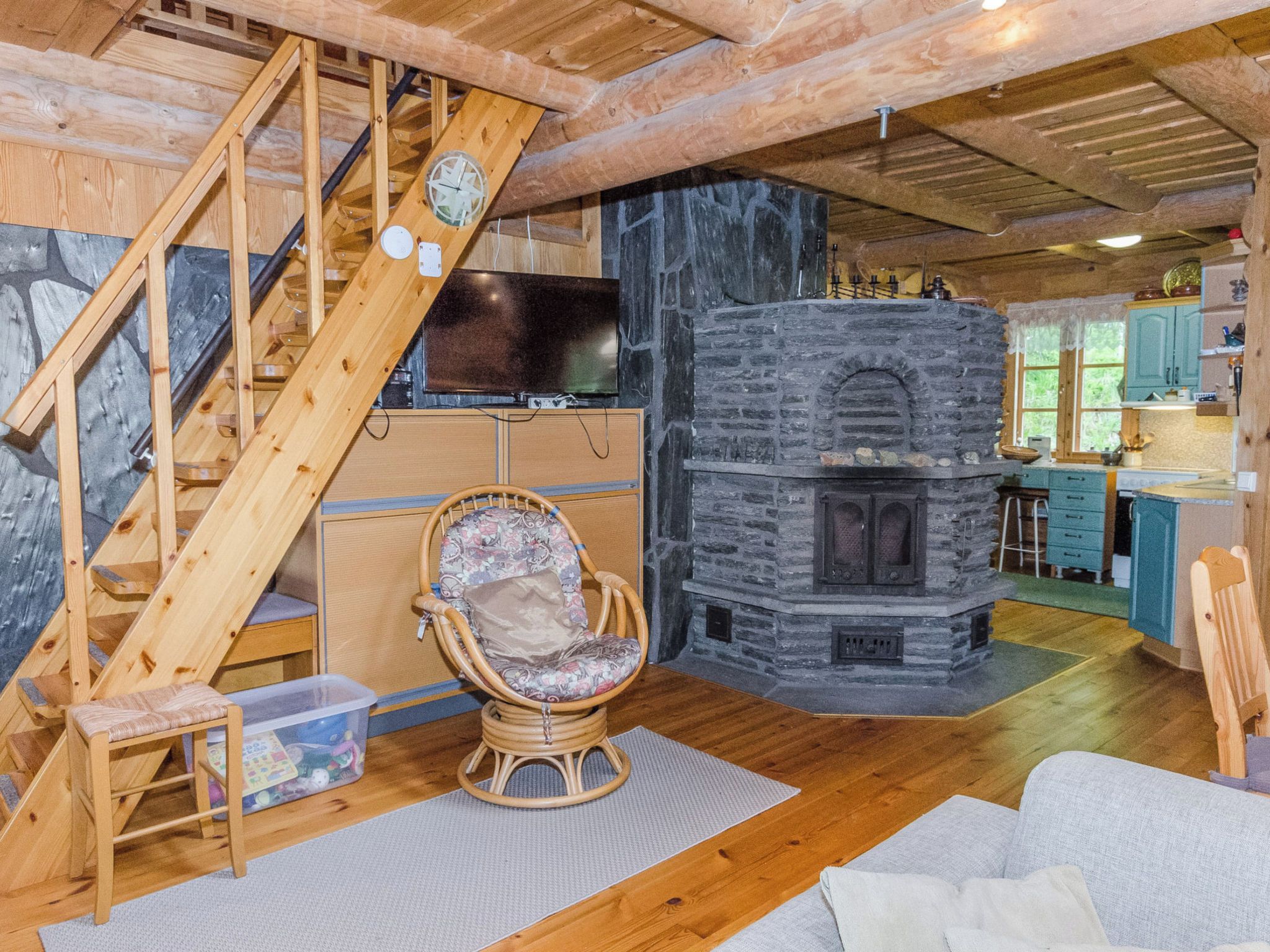 A cozy cabin interior with a stone fireplace, wooden staircase, and a television.