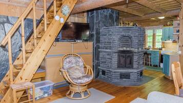 A cozy cabin interior with a stone fireplace, wooden staircase, and a television.