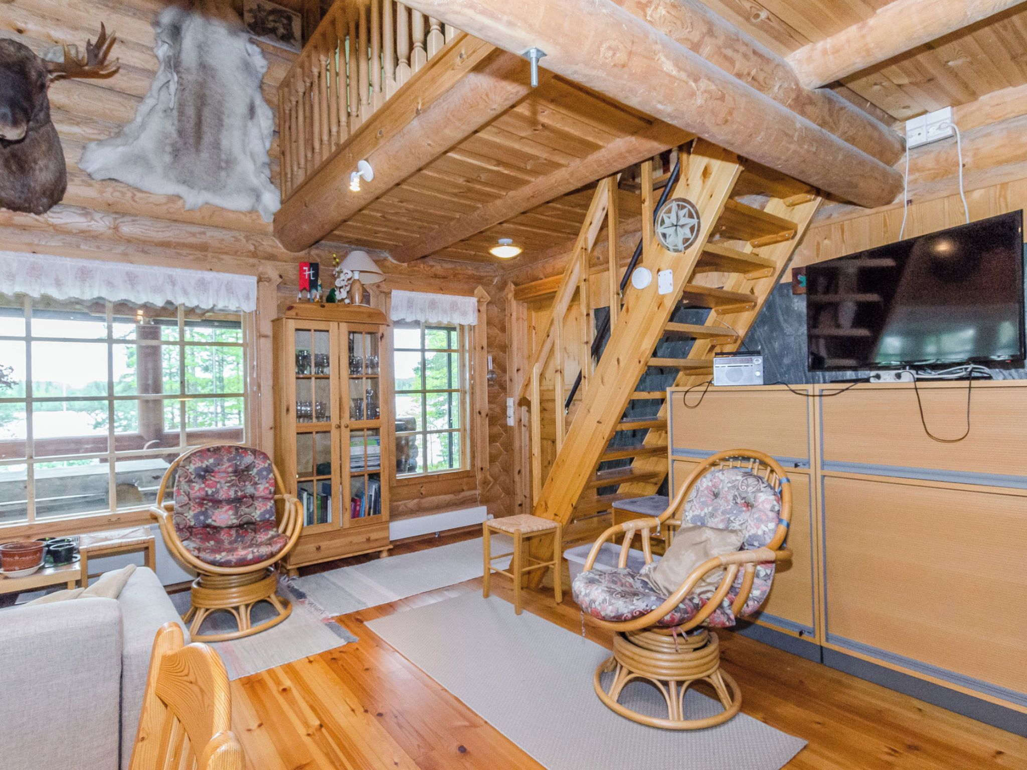 A wooden interior with a staircase, two wicker chairs, a cabinet, and a television.