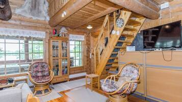 A wooden interior with a staircase, two wicker chairs, a cabinet, and a television.