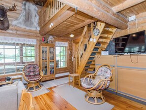 A wooden interior with a staircase, two wicker chairs, a cabinet, and a television.