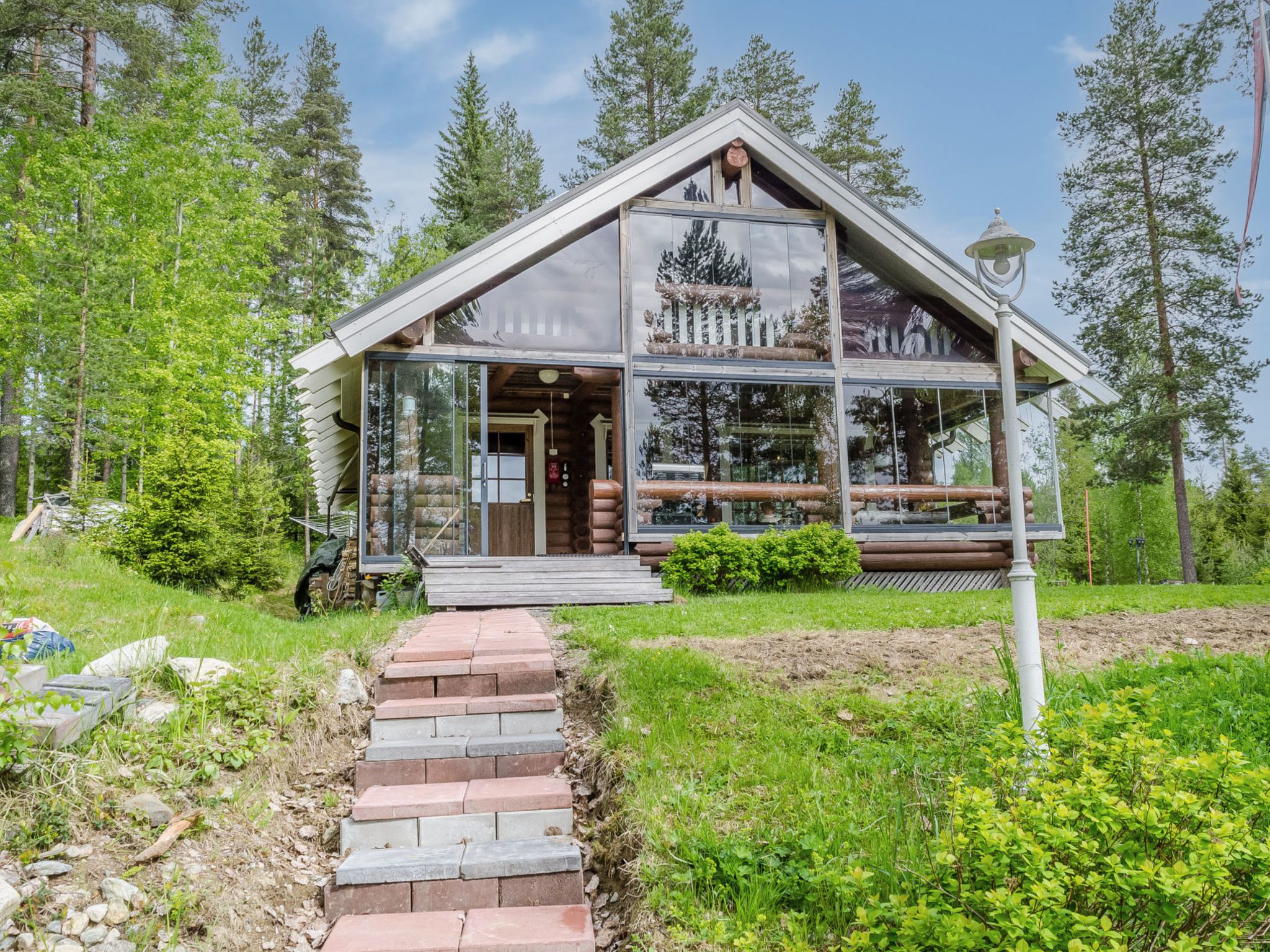 A log cabin with a glass facade, a wooden porch, and a stone pathway leading to the entrance.