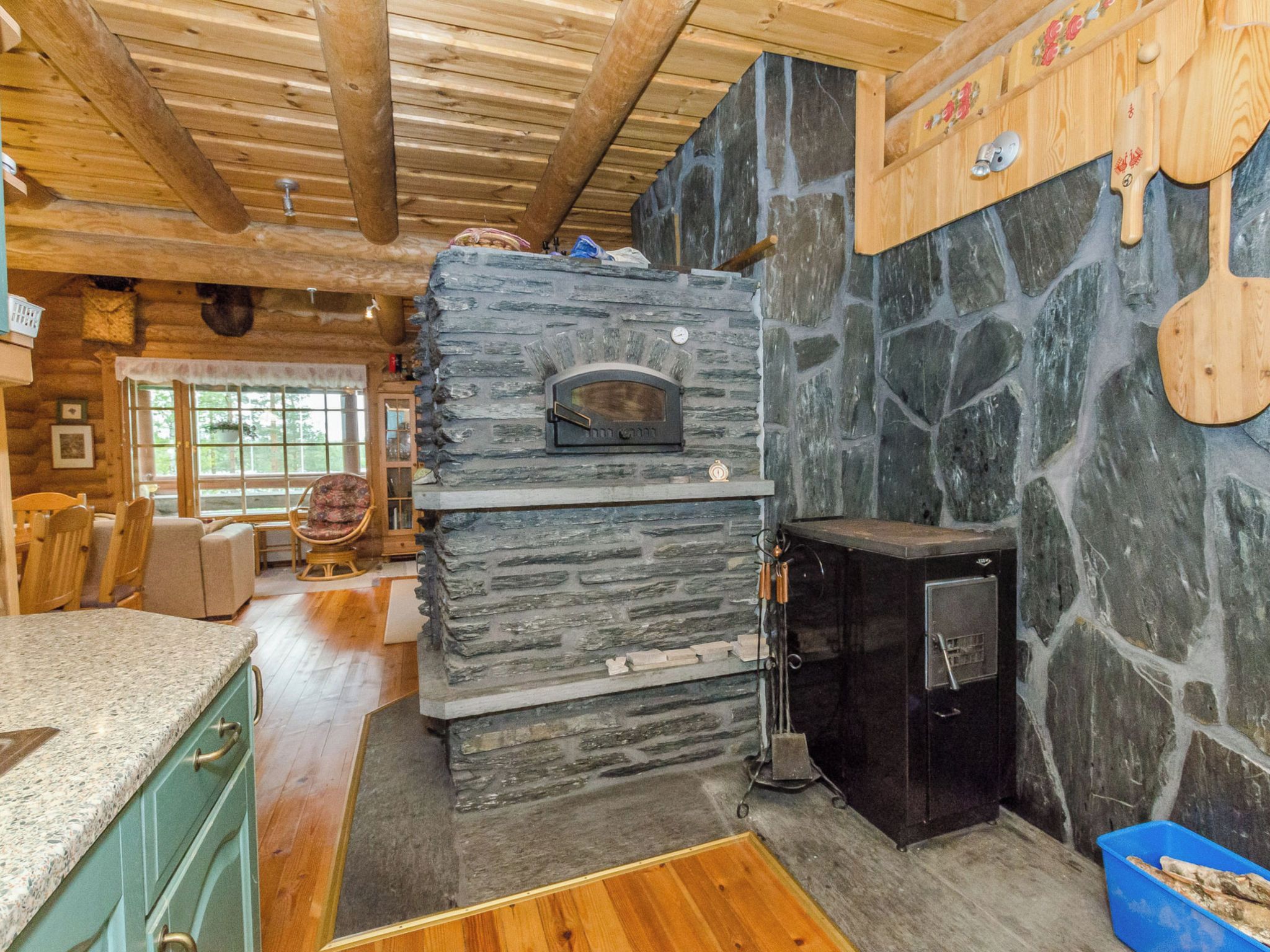 A rustic kitchen with a stone oven, wooden beams, and a stone wall.