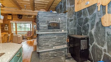 A rustic kitchen with a stone oven, wooden beams, and a stone wall.