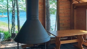A rustic cabin with a wood-burning stove, a bench, and a view of a lake.