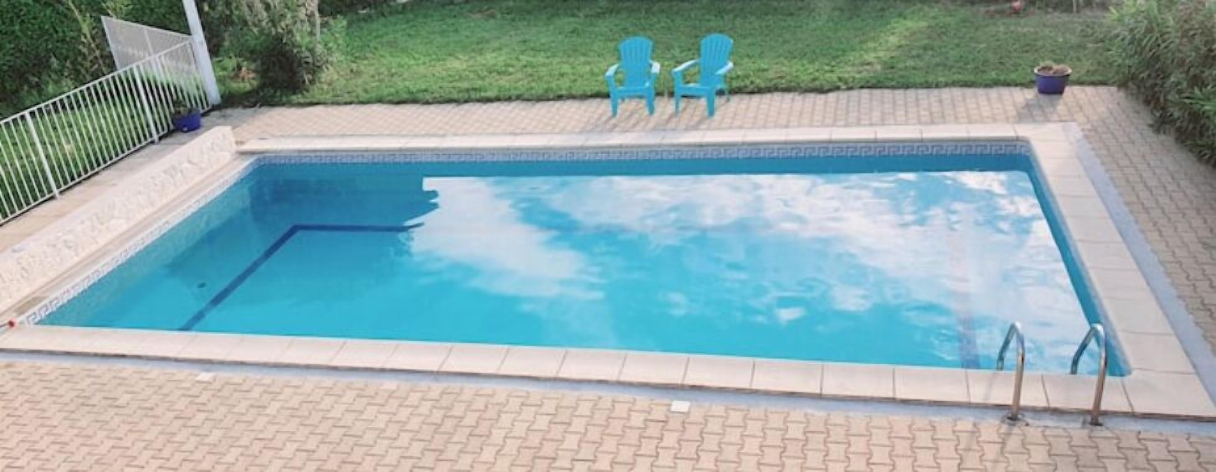 A rectangular swimming pool with a tiled edge, surrounded by a brick patio.