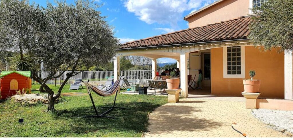 Un espace extérieur abrité comprenant un hamac, des plantes en pot et une petite maison de jeu.