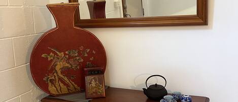 A wooden console table with a mirror above it, a red vase with a floral design, and a small tea set.