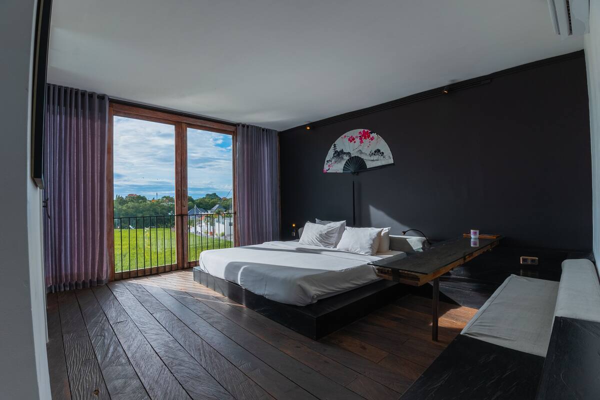 Un dormitorio con una cama grande, un escritorio de madera y vistas a un paisaje verde a través de una puerta corrediza.